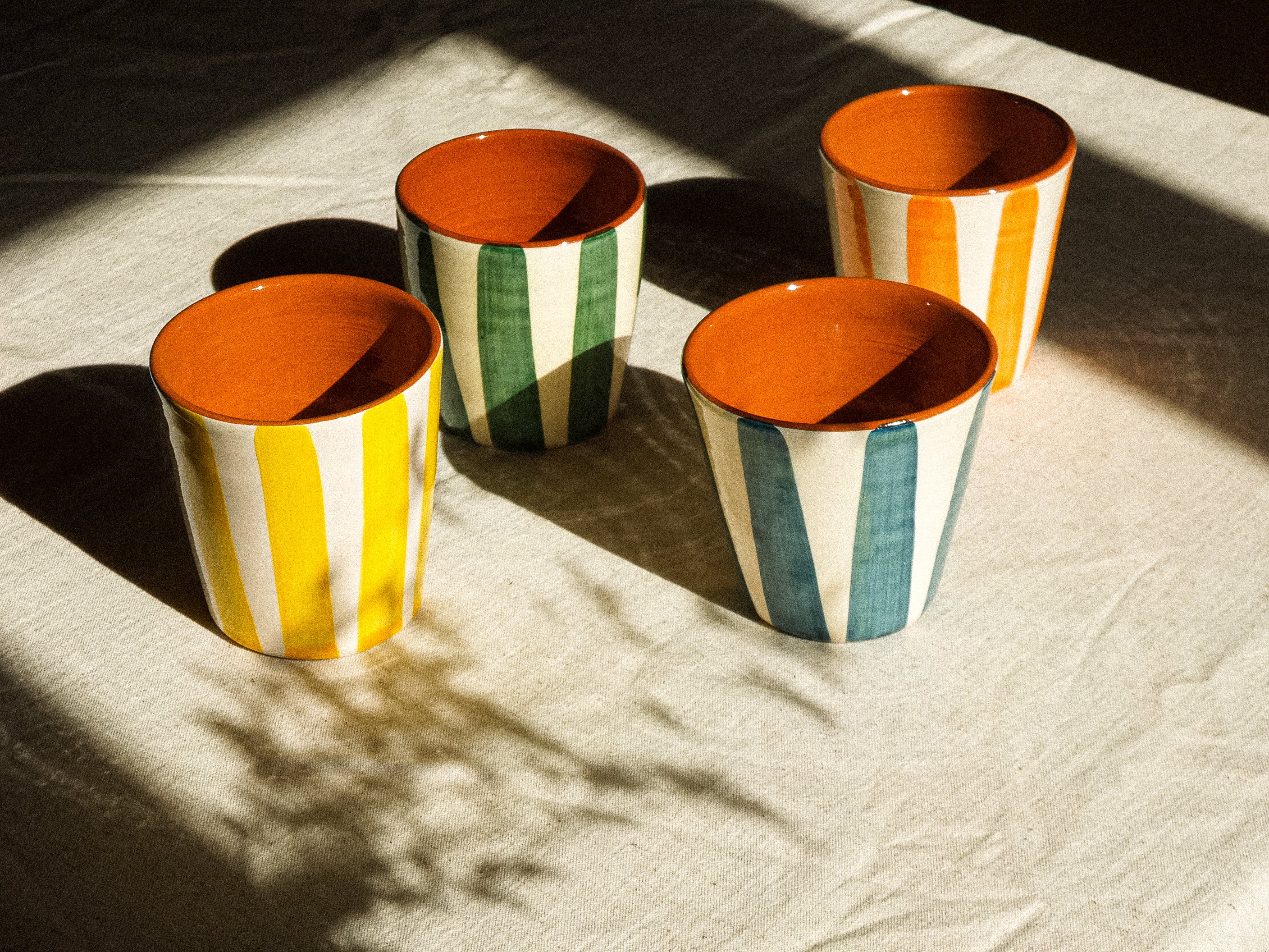 Grandes tasses sans anse en céramique, fabriquée et peinte à la main au Portugal. Blanches avec des rayures colorées, et intérieur terracotta.
